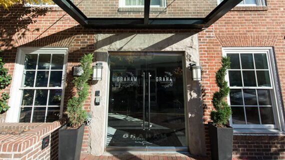Front entrance of The Graham Georgetown hotel with glass doors, brick walls, and potted plants.