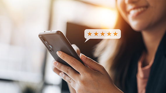 Smiling woman holding a smartphone with a five-star review icon on the screen, representing positive consumer feedback.